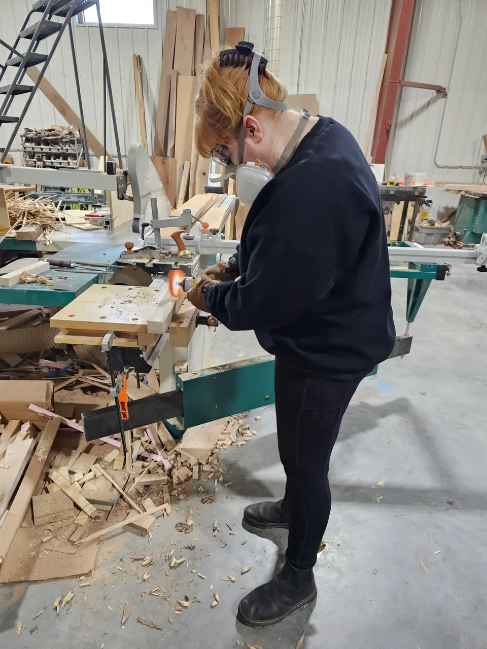 Class student in a respirator and ear protection cutting a board at a workbench in the shop